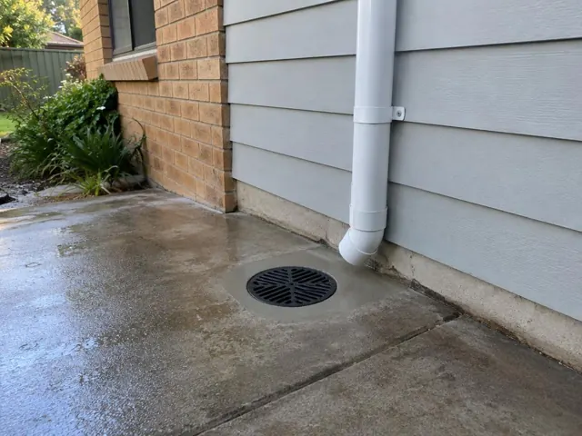 Concrete driveway with a circular drain grate beside a house wall in Westleigh