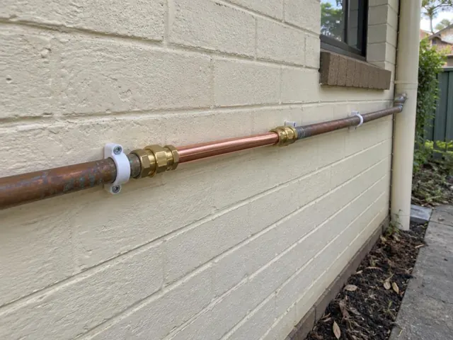 Repaired copper water pipe on a cream brick exterior wall beside a window in Baulkham Hills