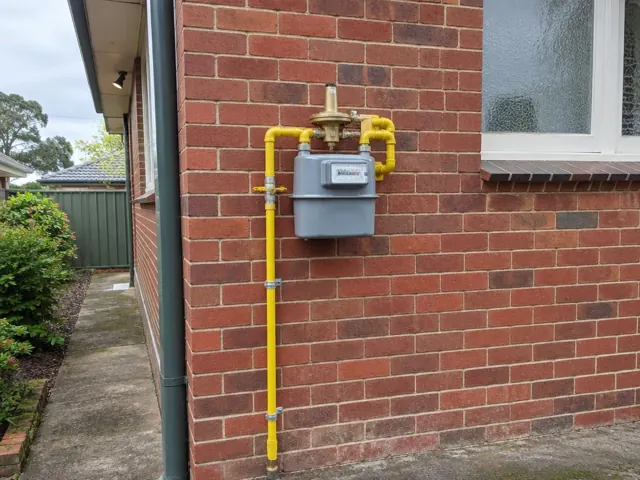 Exterior gas meter with yellow pipework on a red brick wall beside a window in Thornleigh